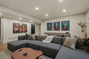 A modern living room with a sectional sofa, a coffee table, and three wall-mounted paintings. - The Rock Haus | Pool, Putt-Putt | Hocking Hills (Laurelville)