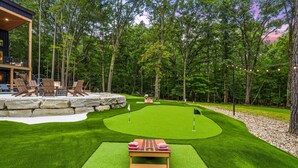 Un campo de golf de césped artificial bien cuidado, con una mesa y sillas de madera, rodeado de un muro de piedra y árboles.