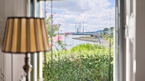 A window view of a river with industrial structures, a lamp, and greenery. - West Beach Cottage - Large Garden and Tay Views (Dundee)