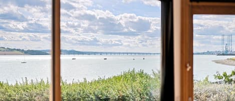 A view through a window of a body of water with boats, a bridge, and industrial structures in the distance.