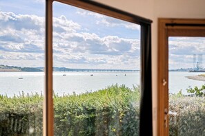 A view through a window of a body of water with boats, a bridge, and industrial structures in the distance.