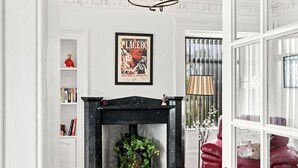 A room with a fireplace, a framed poster on the wall, a bookshelf, and a red armchair. - West Beach Cottage - Large Garden and Tay Views (Dundee)