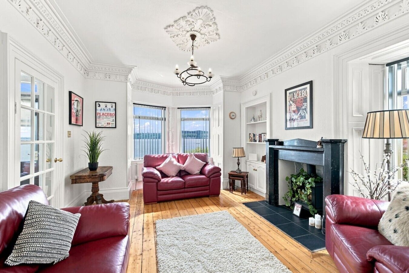 A spacious living room with a fireplace, a red leather sofa, a white rug, and a view of the outdoors through large windows.