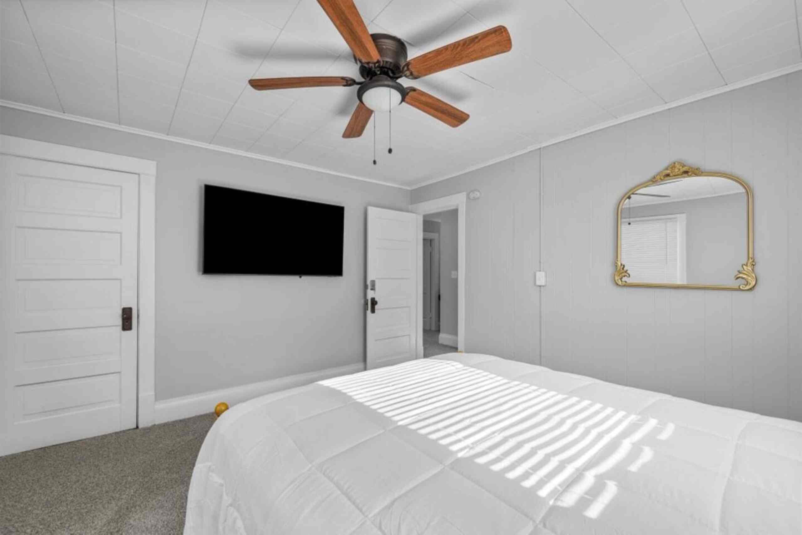 Une chambre dotée d’un ventilateur de plafond, d’un lit recouvert d’une couvre-lit à rayures, d’un téléviseur à écran plat fixé au mur et d’un miroir avec un cadre orné.