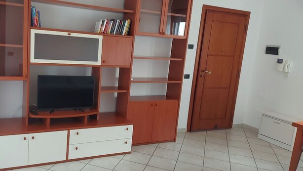 A living room with a TV, wooden shelves, and a door. - Two-room apartment just a few minutes from the Rho Fiera Milan exhibition center, ideal for families and working professionals (Pregnana Milanese)