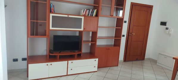 Un soggiorno con televisore, mensole in legno e una porta.