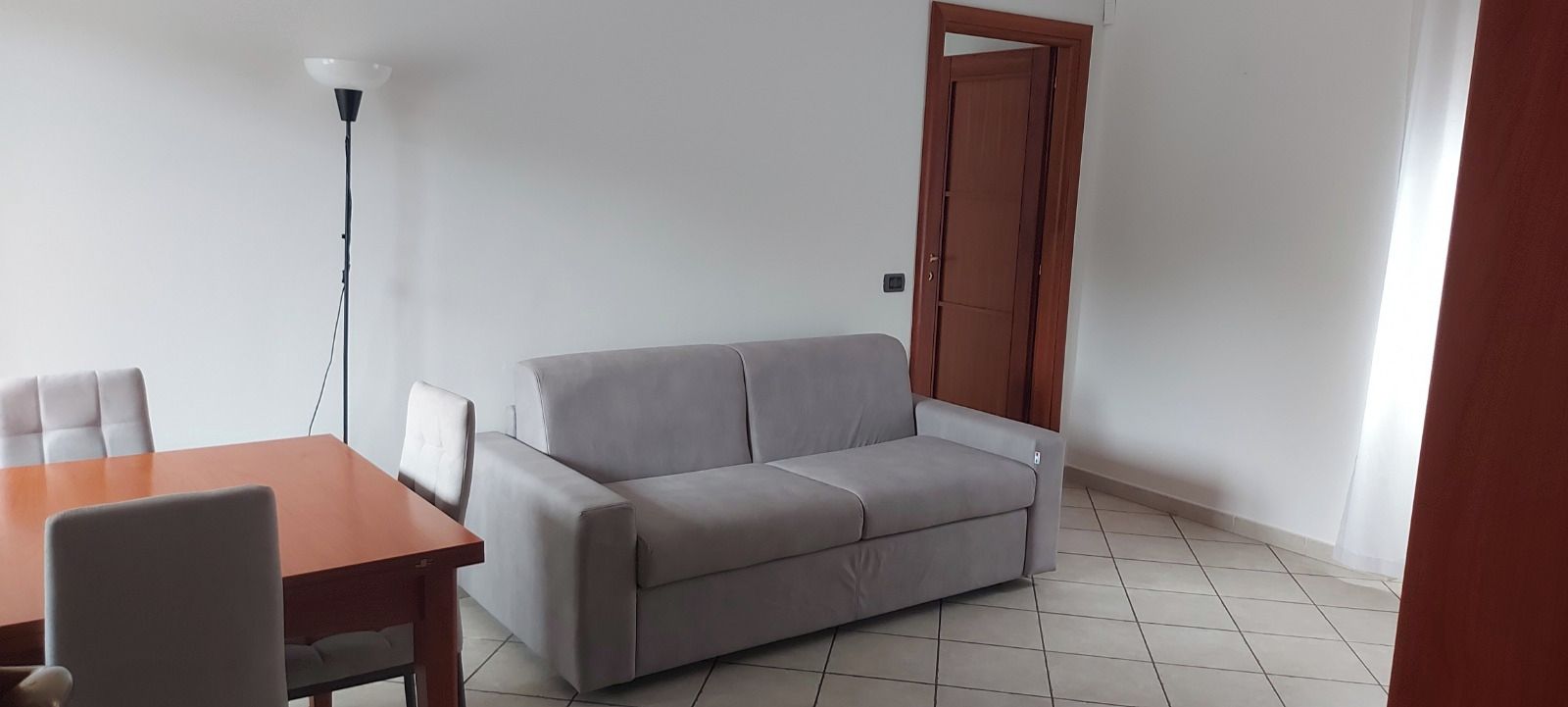 Ein Zimmer mit einer grauen Couch, einem Holztisch und einer Stehlampe.