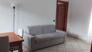 Ein Zimmer mit einer grauen Couch, einem Holztisch und einer Stehlampe.