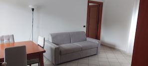 Une pièce avec un canapé gris, une table en bois et un lampadaire.