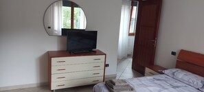 A bedroom with a bed, a TV on a dresser, a mirror, and a door leading to another room.