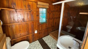 Baño de cabaña de madera con dos inodoros, una ducha y un lavabo.
