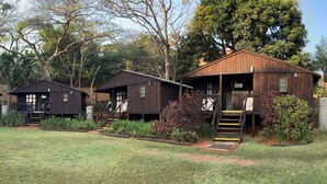 Una hilera de cabañas de madera con escaleras exteriores, rodeadas de jardines y árboles bien cuidados.