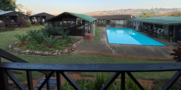 Zona residencial con piscina, cabañas de madera y vistas a un pueblo lejano.