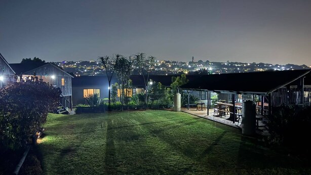 A residential property with a well-maintained lawn, a covered outdoor seating area, and a view of a cityscape at night.