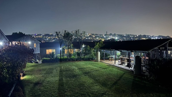 Una propiedad residencial con un césped bien cuidado, un área de estar techada al aire libre y vistas a un paisaje urbano nocturno.