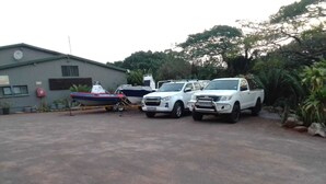 A parking area with three white pickup trucks and a blue boat.