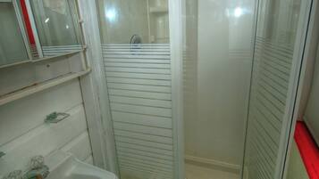 Une petite salle de bain avec une douche, un lavabo et une étagère sur laquelle est posée une serviette.
