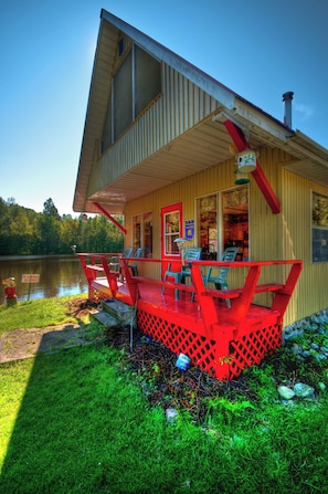 A lakeside building with a sloped roof, a covered deck with chairs, and a sign indicating no responsibility for accidents.