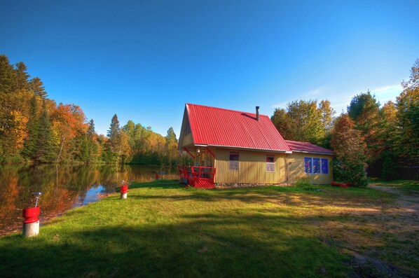 A house with a red roof, situated next to a lake, surrounded by trees.