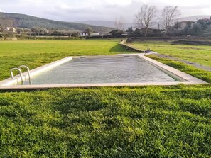 Ein rechteckiger Pool mit einer Leiter an einer Seite, umgeben von einer grünen Wiese, im Hintergrund eine hügelige Landschaft.