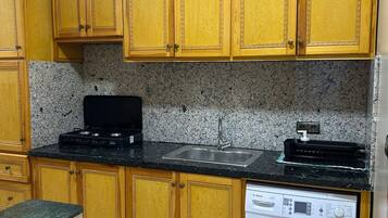 Una cocina con armarios de madera, encimera negra, pileta de acero inoxidable y lavadora Bosch blanca.