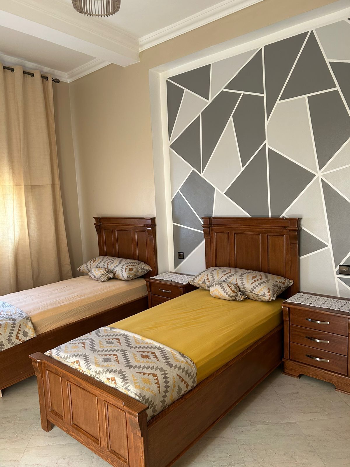 Een slaapkamer met twee houten bedden, een nachtkastje, een dressoir en een wand met een geometrisch patroon.