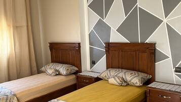 Een slaapkamer met twee houten bedden, een nachtkastje, een dressoir en een wand met een geometrisch patroon.