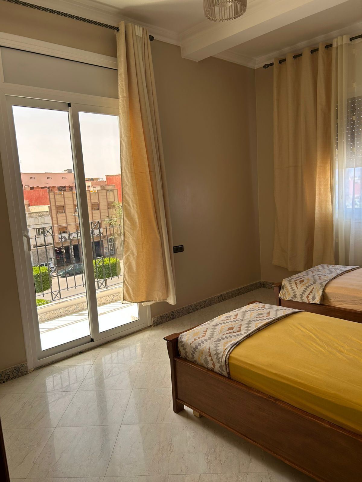 Un dormitorio con un amplio ventanal corredizo que da a un balcón, una cama con colcha estampada y un aplique de techo.