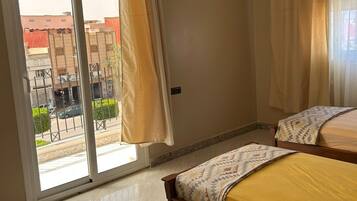 Un dormitorio con un amplio ventanal corredizo que da a un balcón, una cama con colcha estampada y un aplique de techo.