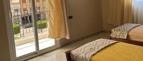A bedroom with a large sliding glass door leading to a balcony, a bed with a patterned bedspread, and a ceiling light fixture.