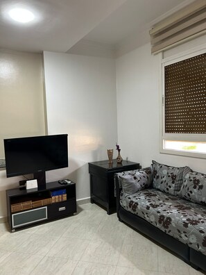 A living room with a flat-screen TV, a black entertainment unit, a sofa, and a window with blinds.