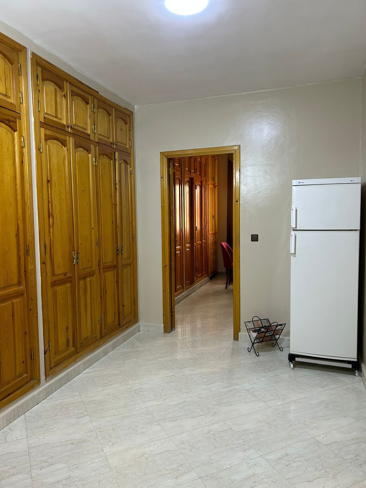A hallway with wooden cabinets, a white refrigerator, and a tiled floor.