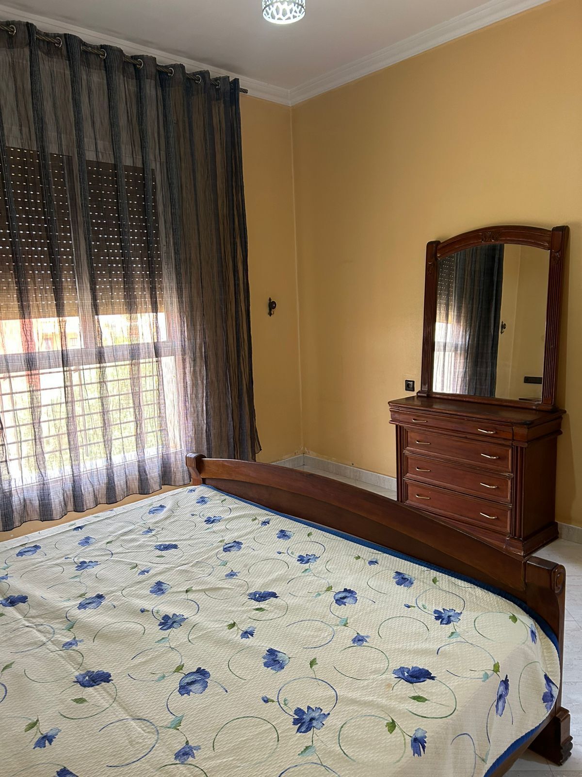 A bedroom with a bed, a dresser, a mirror, and a window with curtains.