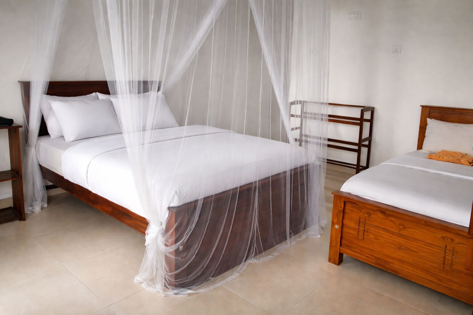 A bedroom with a bed covered by a white canopy, a wooden nightstand, and a bedside table.