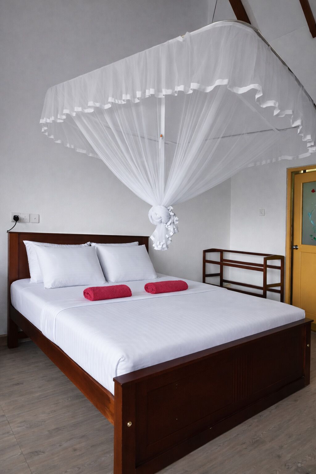 A neatly made bed with white bedding and two red pillows, a wooden headboard, and a white canopy.
