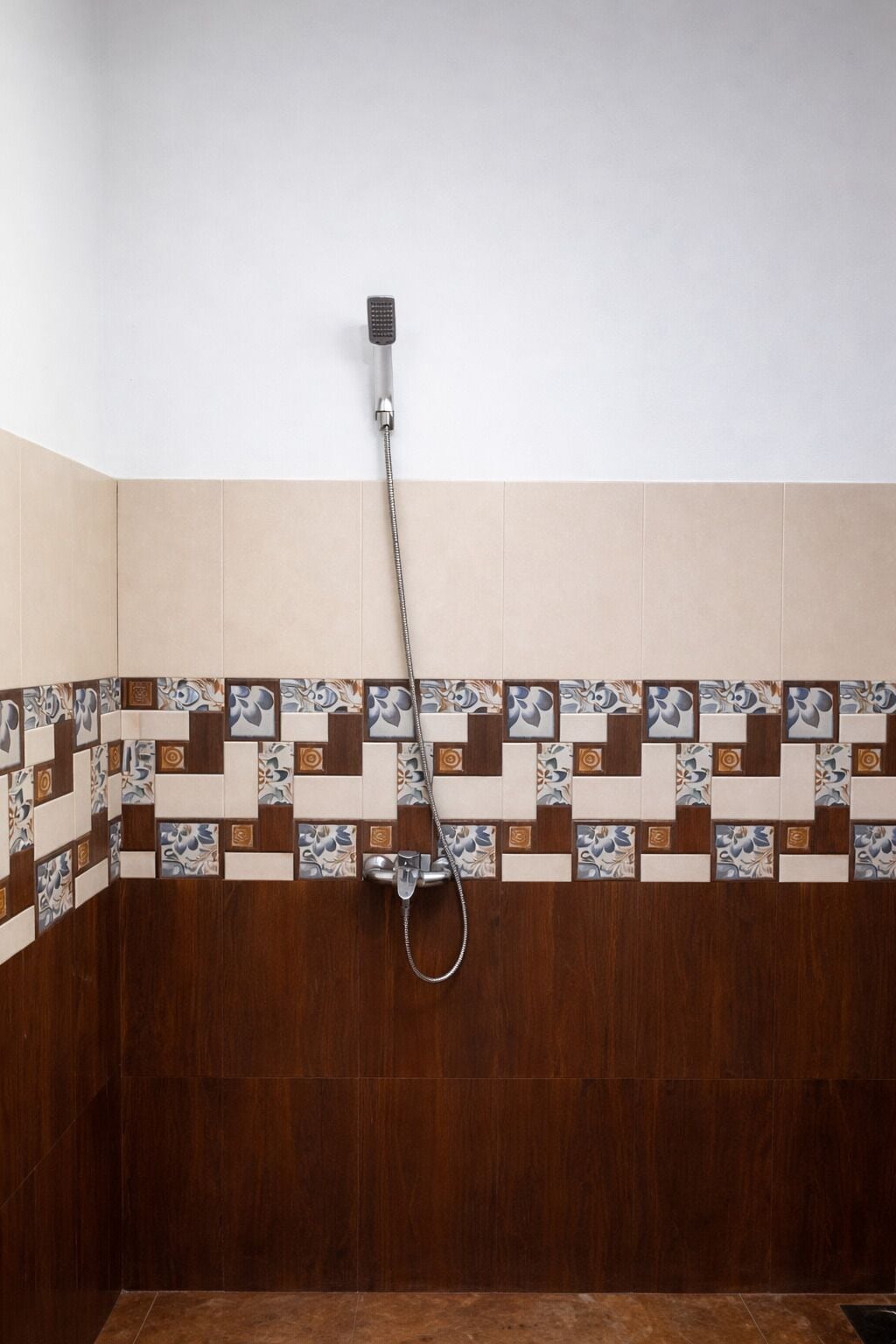 A shower with a handheld showerhead mounted on the wall, a tiled shower floor, and a corner with a wooden wall.