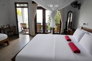 A hotel room with a large bed, a desk, and a chair. There is a balcony with a view of greenery. - Amado Homestay Ella (Badulla)