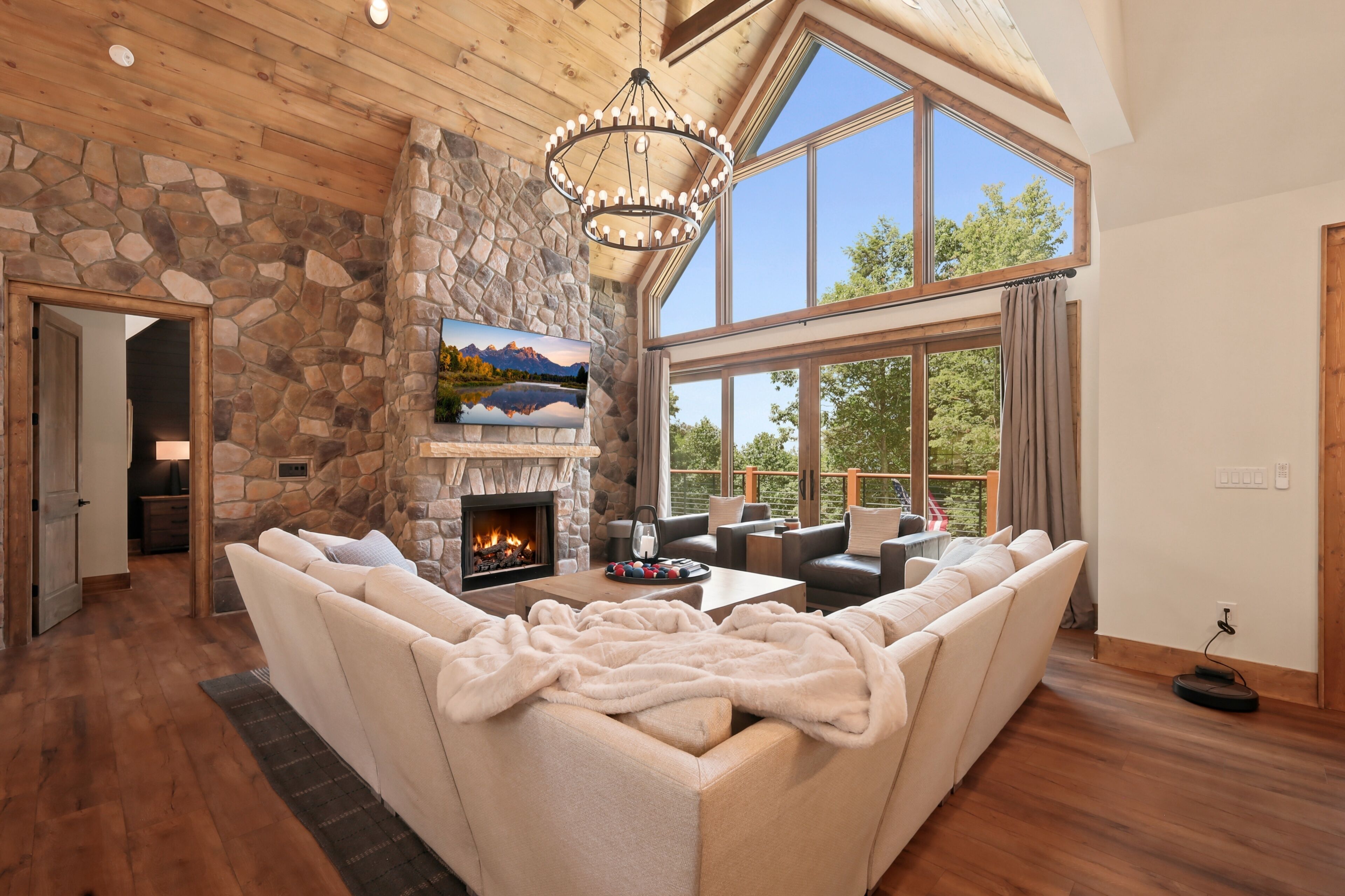 A spacious living room with a stone fireplace, comfortable seating, and large windows offering a view of the outdoors.