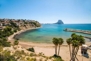 Un pueblo costero con playa, mar azul turquesa y un acantilado imponente.