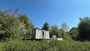 A small, single-story mobile home with a door and a window, surrounded by dense greenery and trees. - Elegant Hideaway| Twin baths under the stars (Doddington)