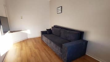 A room with a dark-colored sofa, a flat-screen TV mounted on the wall, and a wooden floor.