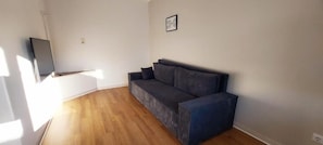A room with a dark-colored sofa, a flat-screen TV mounted on the wall, and a wooden floor. - Familienapartments Wildemann (Wildemann)
