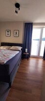 A bedroom with a bed, a bedside table, a lamp, and a view of the outdoors.