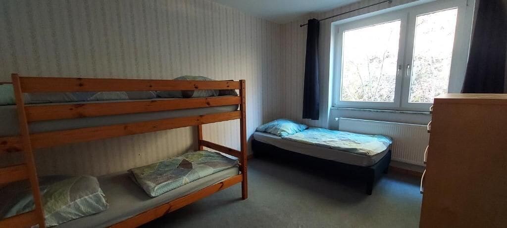 Una habitación con literas y una cama individual, una ventana con cortinas y un radiador.