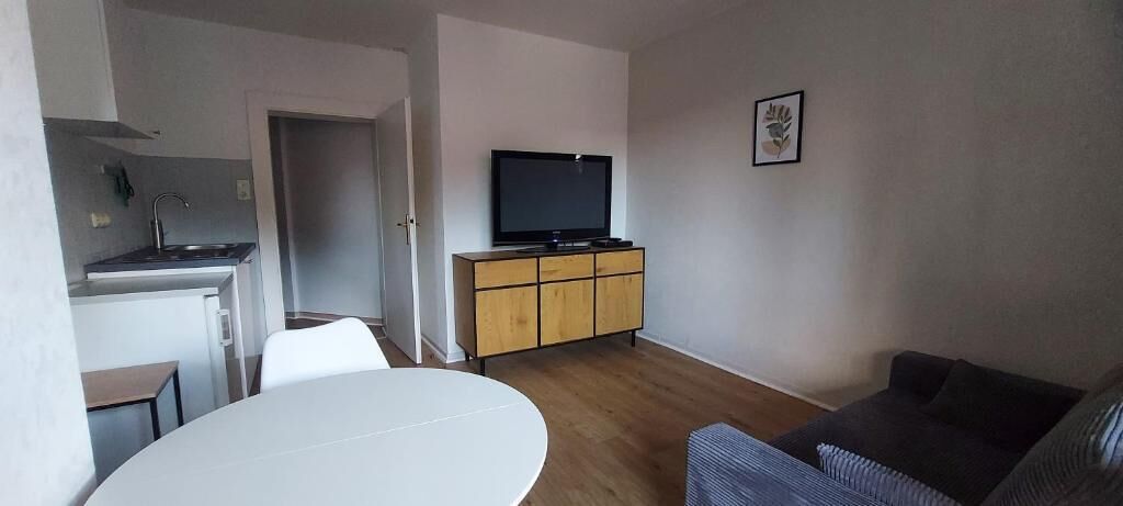 Ein gemütlicher Wohnbereich mit Küchenzeile, einem Esstisch, einer Couch und einem Fernseher auf einem Schrank.