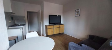 Un espacio habitable compacto con kitchenette, una mesa de comedor, un sofá y un televisor sobre un mueble.