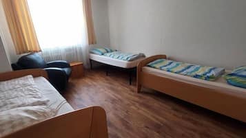 A room with two wooden beds, a chair, and a window with curtains.