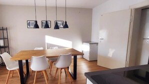A dining area with a wooden table and white chairs, a black hanging light fixture, and a radiator on the wall.