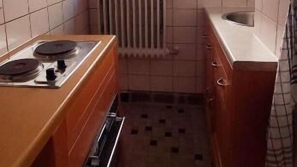 A small kitchen with a window, a radiator, and a tiled floor.
