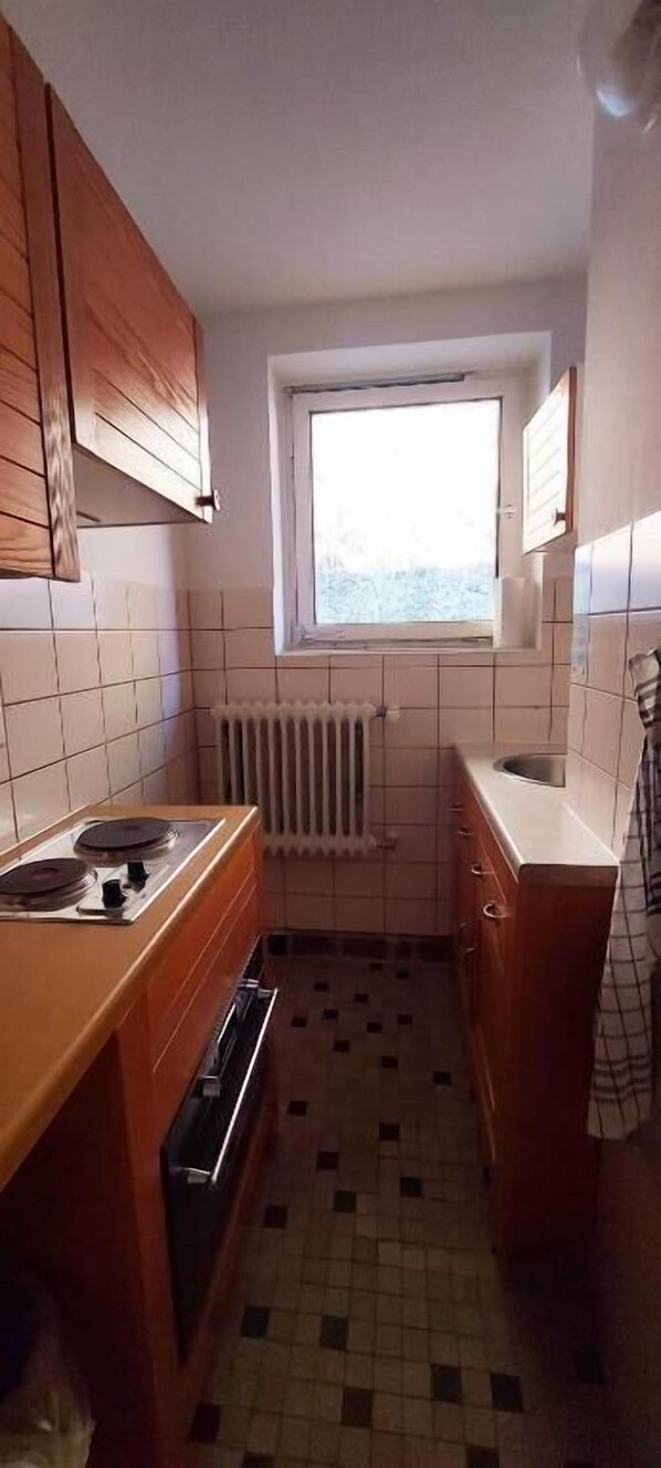 A small kitchen with a window, a radiator, and a tiled floor.